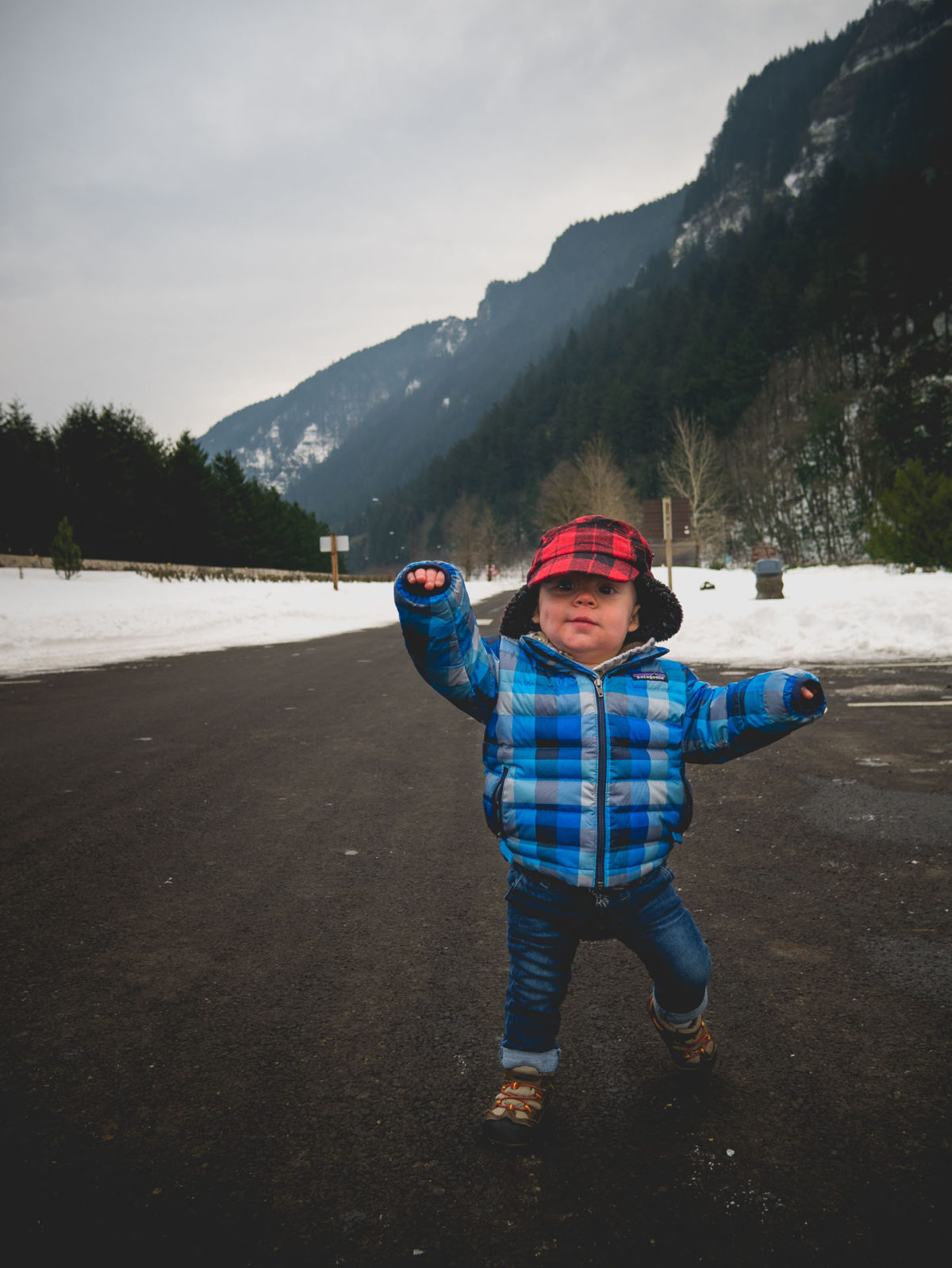 Toddler walking down road with snow and forests in the background