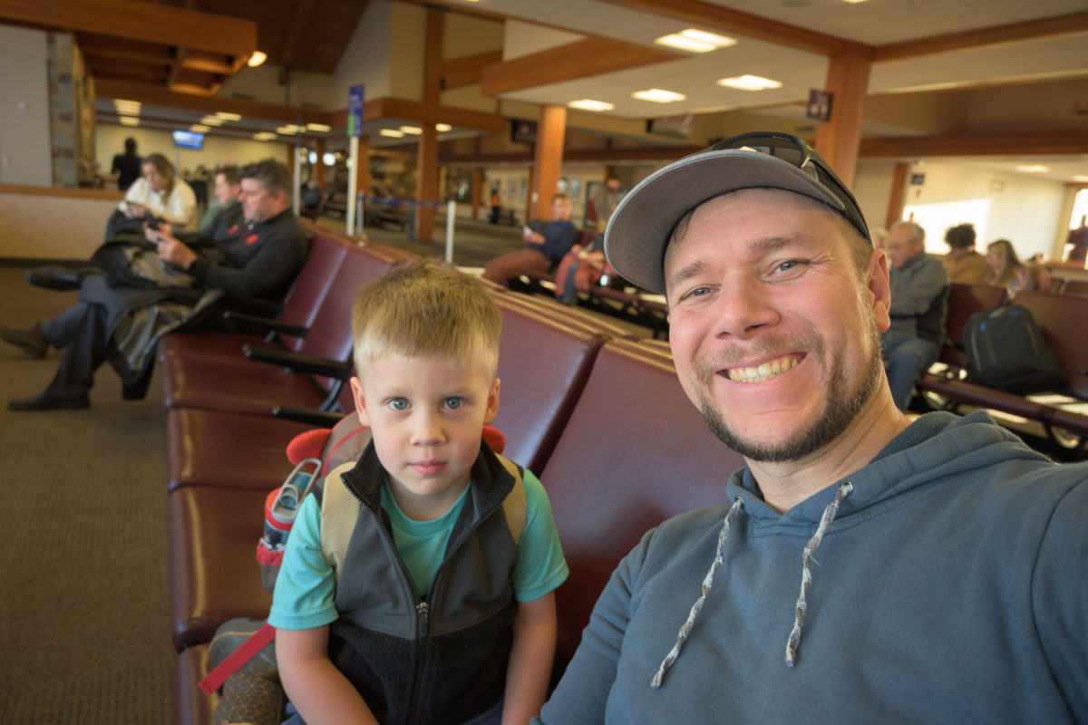 A boy and his father sitting at an airport posing for a picture