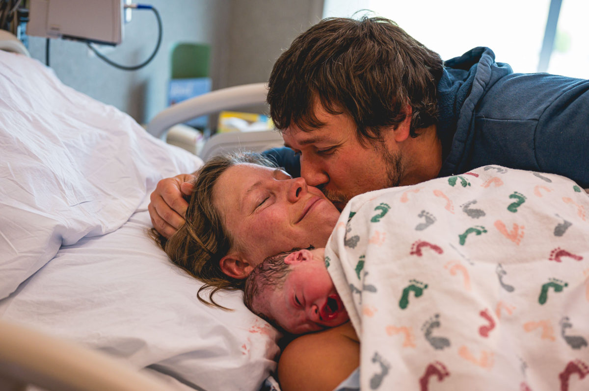 Husband kisses wife as she holds their newborn child just after birth