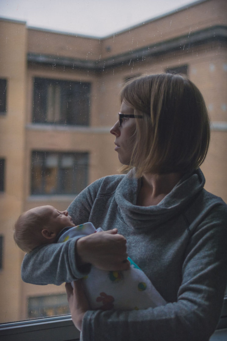 Mother holds newborn child while looking out a window