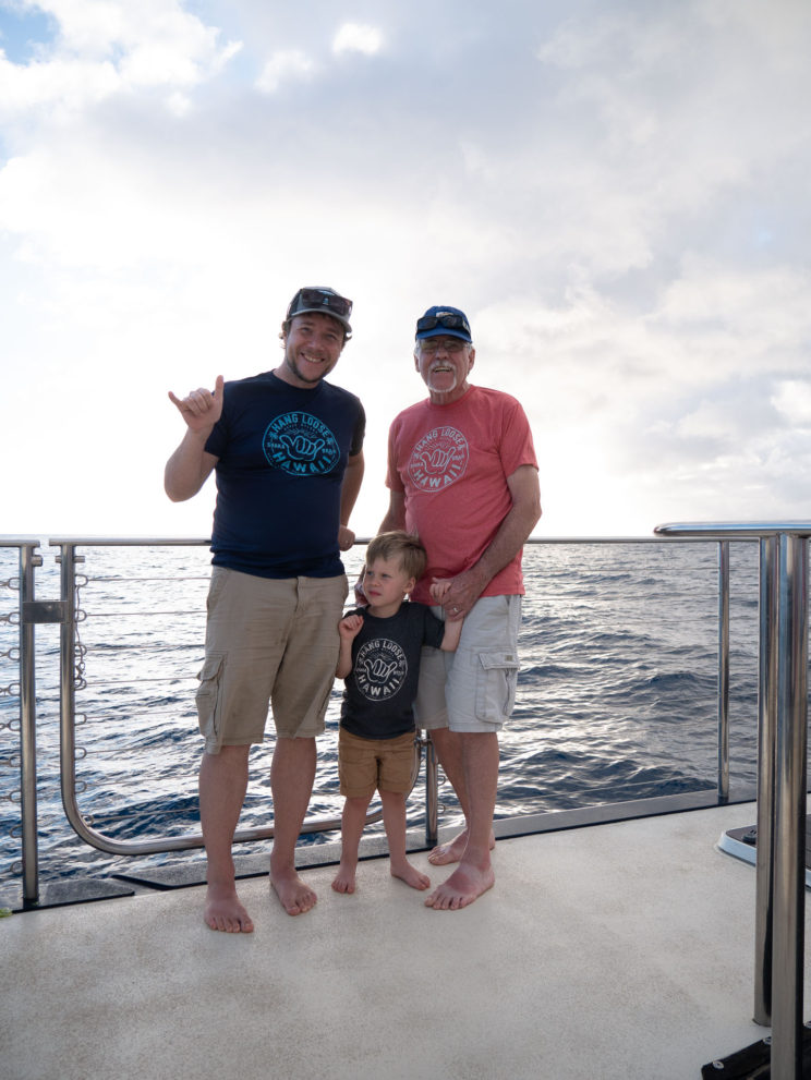 Three generations holding up the shaka hand gesture on a boat